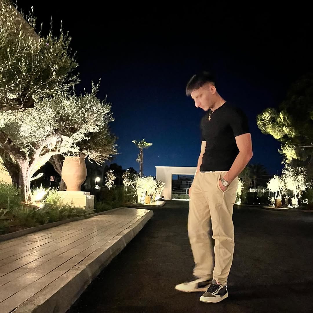 Standing in a lit outdoor garden at night, illuminated olive trees and terracotta pot
